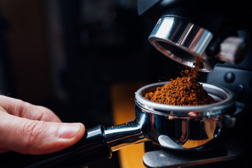 Ground coffee pouring into a portafilter with a grinder, closeup