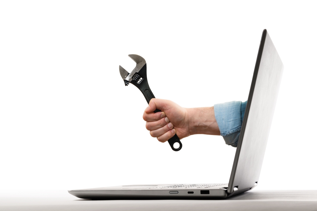 The human hand with black wrench stick out of a laptop screen.